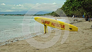 Yellow surfboard on beach with red text surf rescue emergency on a beach