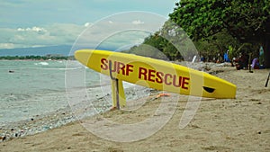 Yellow surfboard on beach with red text surf rescue emergency on a beach