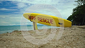 Yellow surfboard on beach with red text surf rescue emergency on a beach