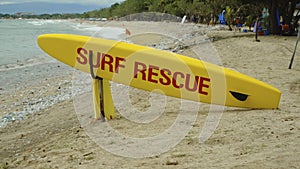 Yellow surfboard on beach with red text surf rescue emergency on a beach