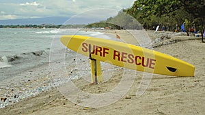 Yellow surfboard on beach with red text surf rescue emergency on a beach