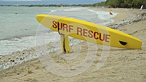 Yellow surfboard on beach with red text surf rescue emergency on a beach