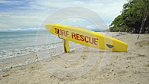 Yellow surfboard on beach with red text surf rescue emergency on a beach