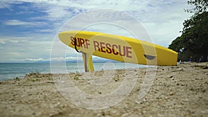 Yellow surfboard on beach with red text surf rescue emergency on a beach