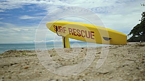 Yellow surfboard on beach with red text surf rescue emergency on a beach