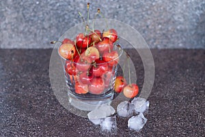 Yellow sweet cherries in a whiskey glass, ice cubes and a bottle of whiskey against a stone background. A refreshing cold cocktail