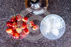 Yellow sweet cherries in a whiskey glass, ice cubes and a bottle of whiskey against a stone background. A refreshing cold cocktail