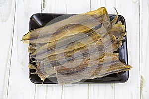 Yellow tabby Latin: Selaroides leptolepis dried folded in rows on a black rectangular plate with a wooden table background.