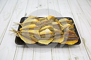 Yellow tabby Latin: Selaroides leptolepis dried folded in rows on a black rectangular plate with a wooden table background. Food