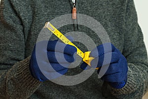 Yellow tape measure in male hands in blue gloves.