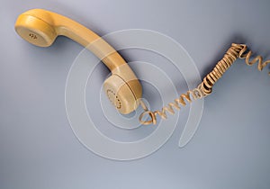 Yellow telephone receiver with twisted cord from an old antique rotary phone on blue background. Plastic removed handset