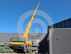 Yellow telescopic crane on a large truck working outside a modern gray building