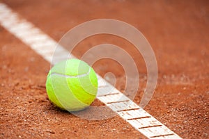 A yellow tennis ball lies on the clay court