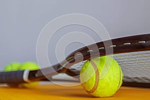 Yellow tennis ball lying under the racket strings at the yellow background