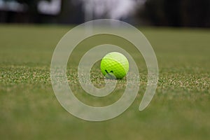 a yellow tennis ball sits in the grass near a golf hole