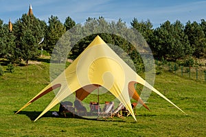Yellow tent or marquee with chairs in green field. Outdoor activities, events, awning for relaxation