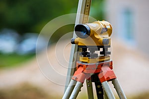 Yellow theodolite on a tripod and a ruler with a blurred background. Geodetic measurements.