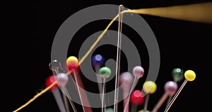 Yellow thread passing through the eye of the needle, close-up against the background of colorful pins