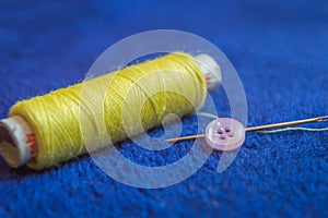 A yellow thread roll with a needle and a button on a blue background