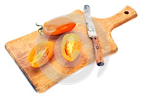 Yellow tomatoe with half slices and old knife on wooden board.