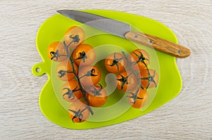 Yellow tomatoes cherry on branch, knife on cutting board on wooden table. Top view