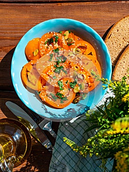 Yellow tomatoes salad with rye bread slices in blue ceramic bowl top view. Ripe fresh colorful vegetables mixed greens