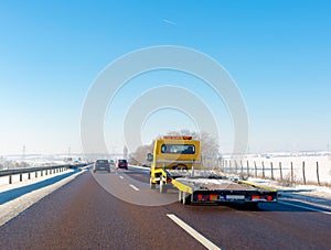 Yellow tow truck with empty platform moves on highway in winter