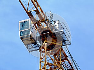 yellow tower crane boom and vertical tower body. clear blue sky. white operating cabin