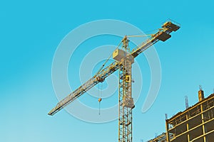 Yellow tower crane at construction site on blue sky background toned