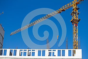 Yellow tower crane near new building over blue sky, selective focus