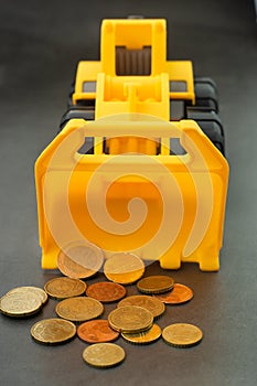 Yellow toy bulldozer, excavator carrying a lot of money - euro cent coins on dark background. Money digging, subsidies from Europe