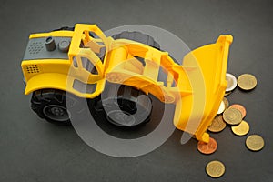 Yellow toy bulldozer, excavator carrying a lot of money - euro cent coins on dark background. Money digging, subsidies from Europe