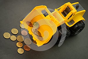 Yellow toy bulldozer, excavator carrying a lot of money - euro cent coins on dark background. Money digging, subsidies from Europe
