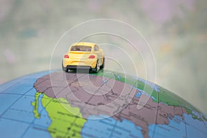 A yellow toy car is traveling around the globe. Back view The car is located on the American continent of the world map. The conce