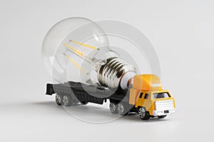 A yellow toy truck with a trailer carries a modern energy-saving LED bulb. Concept of transport services and fast delivery of