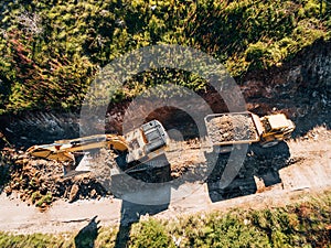 Yellow tracked tractor loads a quarry vehicle with sand. Aerial view