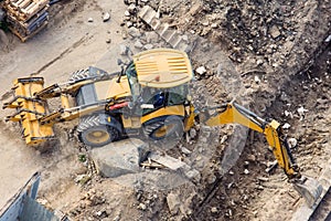 Yellow tractor with a bucket and back and front, digging a trench at a construction site. View from above