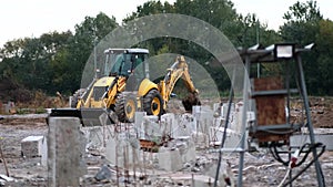 A yellow tractor bulldozer excavator digs a trench with a bucket between reinforced concrete piles.