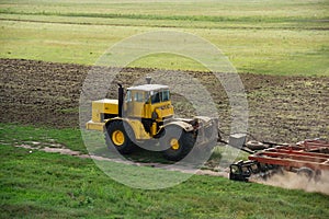 Yellow tractor cultivating green field in autumn