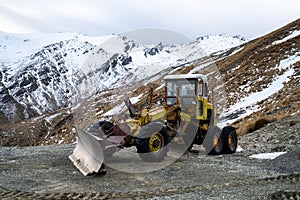 A yellow tractor on a deserted road covered with snow surrounded in South Island, New zealand