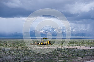 Yellow Tractor with plow working on field with grass