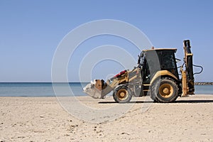Yellow tractor rides on the beach along the sea