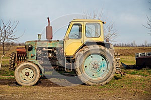 A yellow tractor stands in the countryside. Agriculture and farming.An old tractor