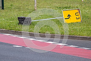 Yellow traffic sign lying down on the grass at a street and signalizes a redirection on European streets to recalculate navigation