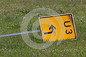 Yellow traffic sign lying down on the grass at a street and signalizes a redirection on European streets to recalculate navigation