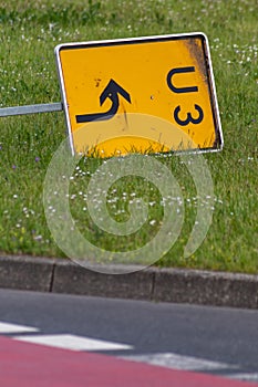 Yellow traffic sign lying down on the grass at a street and signalizes a redirection on European streets to recalculate navigation