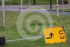 Yellow traffic sign lying down on the grass at a street and signalizes a redirection on European streets to recalculate navigation