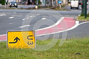 Yellow traffic sign lying down on the grass at a street and signalizes a redirection on European streets to recalculate navigation