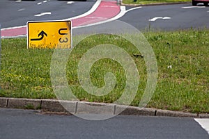Yellow traffic sign lying down on the grass at a street and signalizes a redirection on European streets to recalculate navigation