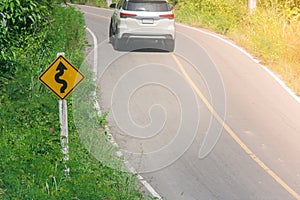 Yellow traffic sign `maze traffic` on green bush beside the road with car and sunlight background.